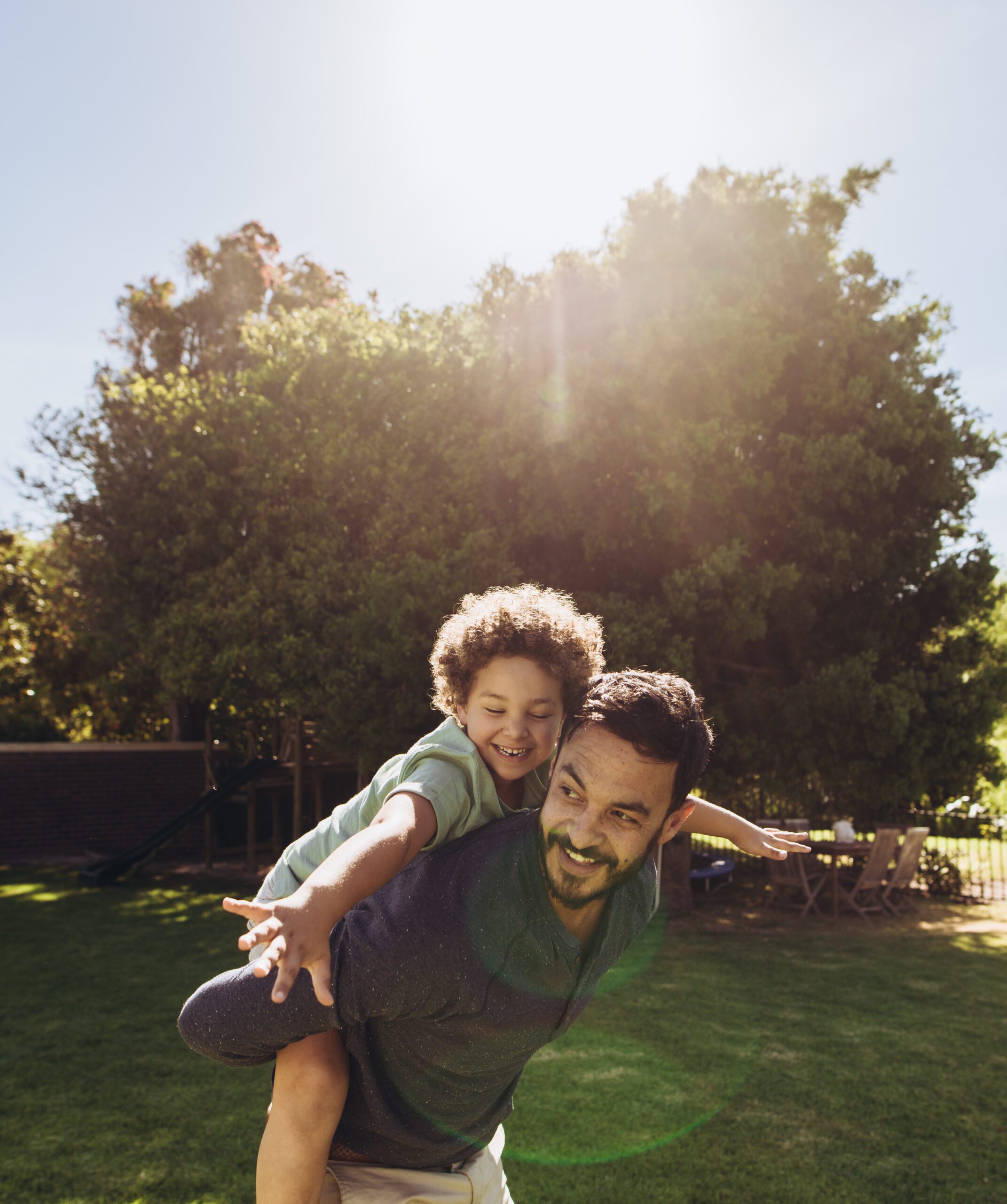 Man walking in a park carrying his son on his back on a sunny day