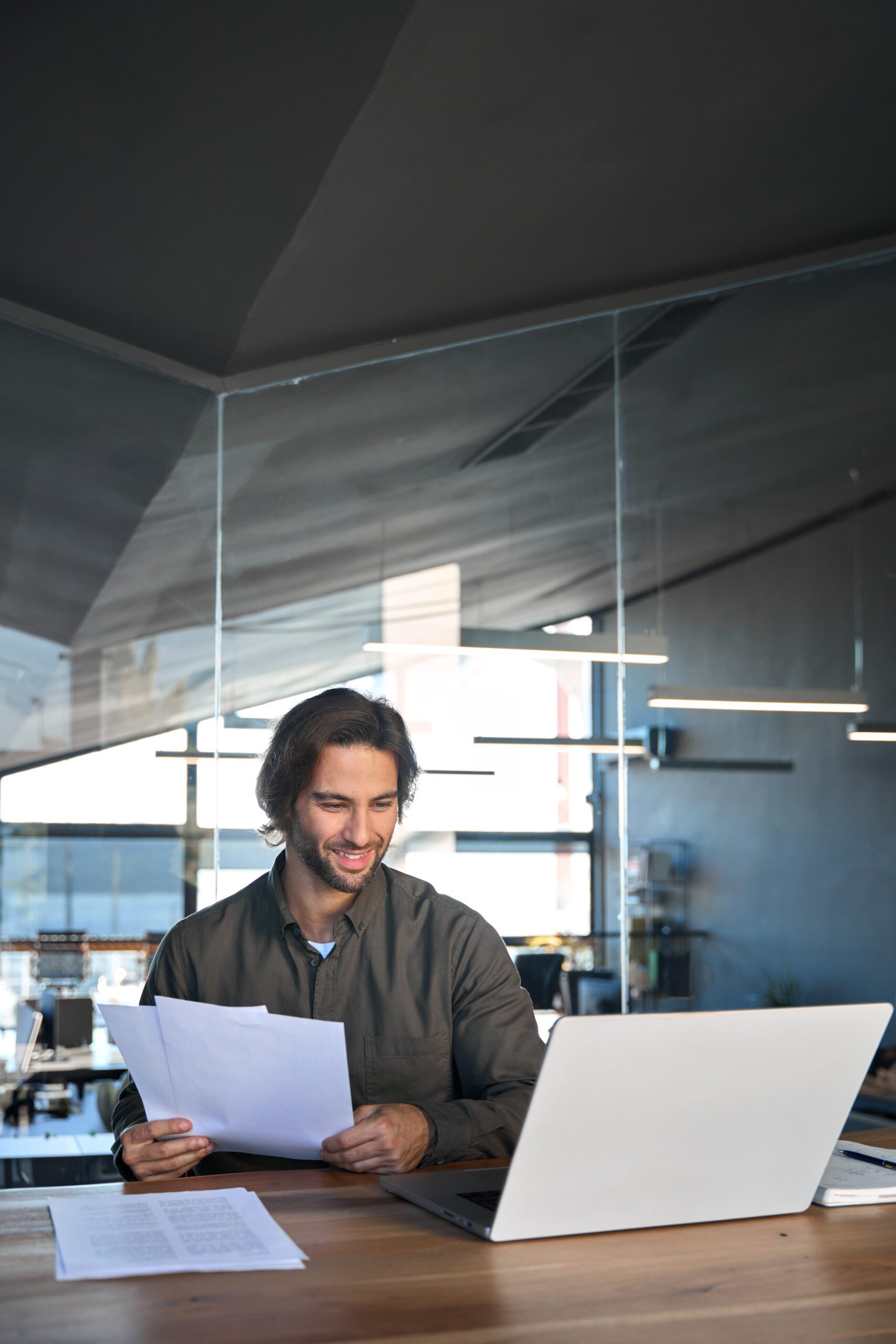 Happy young businessman holding documents using a laptop computer at work.